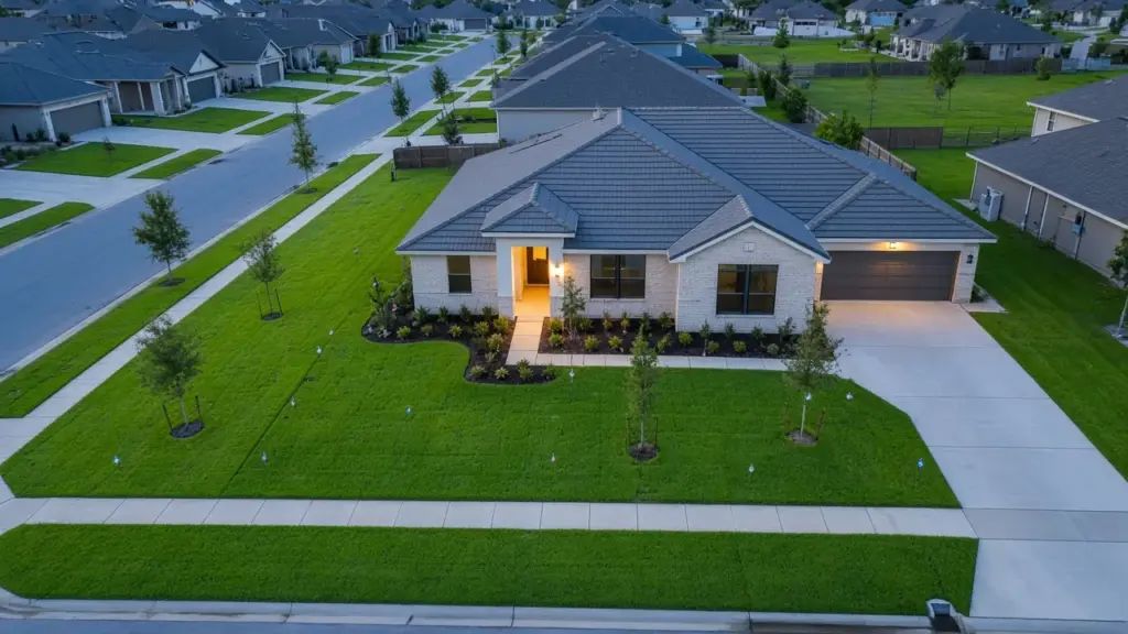 A newly built suburban home with fresh sod, young trees, and new sprinkler heads marked by small flags